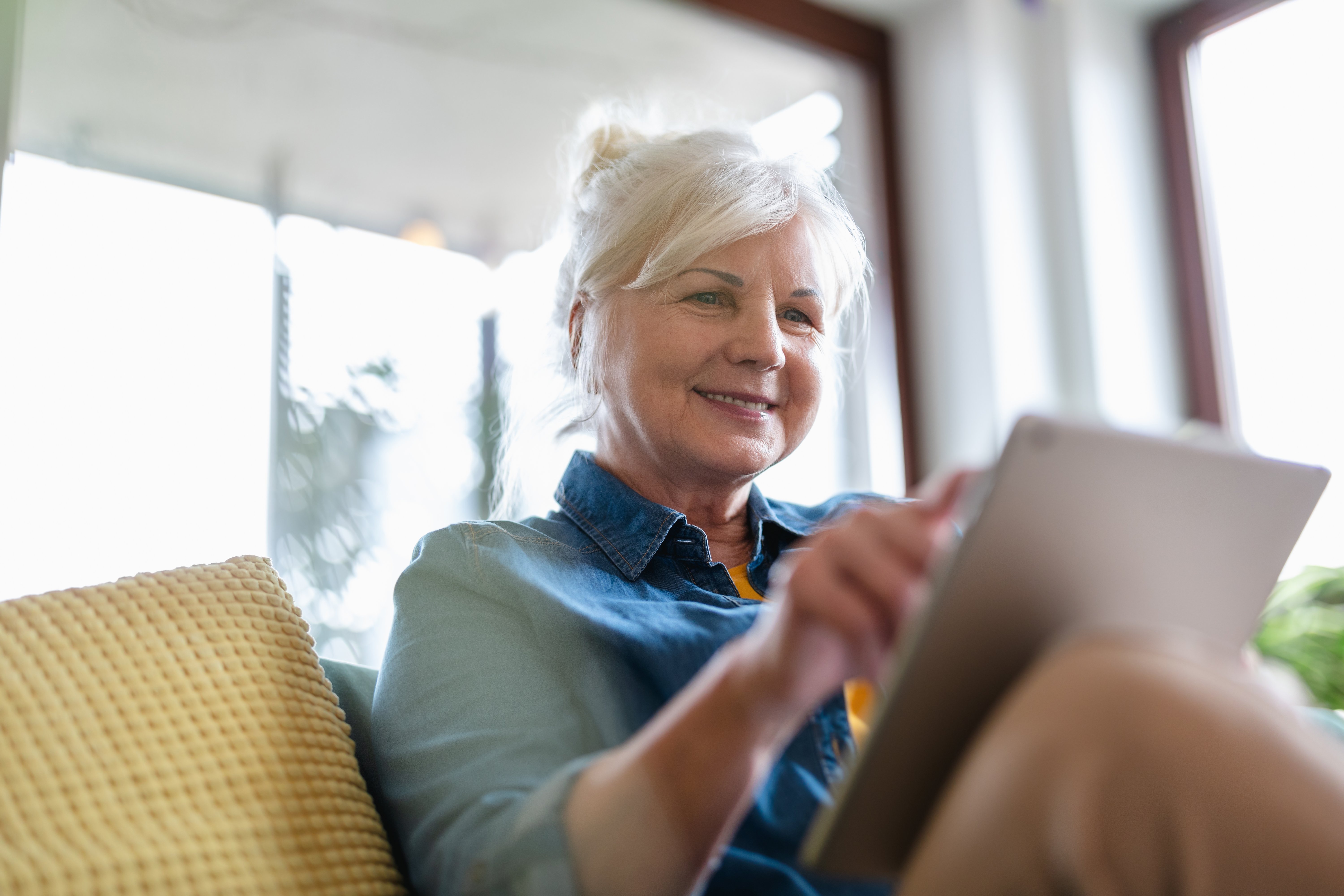 female-european-elderly-indoor-using-digital-tablet-while-sitting-on-sofa-web (1)